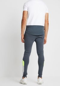 Grijze sweatpants met een slim fit, voorzien van neon groene en lichtgrijze accenten. Gecombineerd met een wit T-shirt en lichte sneakers.