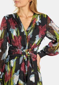 Vestido envolvente floral hecho de tela negra transparente. Presenta patrones florales en rojo y azul, un escote en forma de V, mangas largas y una cintura atada.