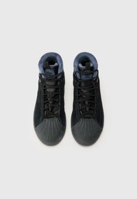 Des chaussures de sport montantes noires avec une tige en suède texturé, un embout en caoutchouc et une doublure en polaire bleue douce autour du col.