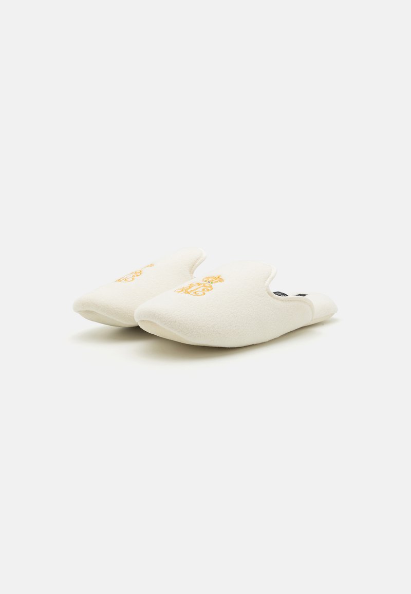 Chaussons en polaire blanche avec un design courbé et un emblème doré brodé à l'avant, offrant une apparence douce et confortable.