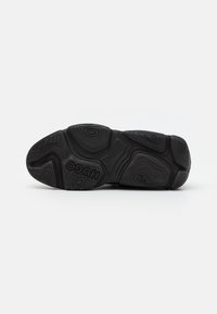 Sole nera di sneaker con motivi ondulati testurizzati e un logo in rilievo. Il design presenta contorni vari per trazione e grip.