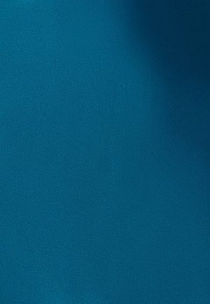 Een glimlachende vrouw fietst op een zwarte fiets met manden in een stadspark op een zonnige dag.