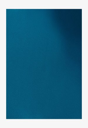 Een glimlachende vrouw fietst op een zwarte fiets met manden in een stadspark op een zonnige dag.