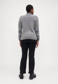 Siv sweater z visokim ovratnikom, ki ima modre in sive črte na rokavih. V kombinaciji z črnimi hlačami in debelimi črnimi škornji.