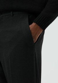 Zwarte broek met rechte snit, zijzakken en een gladde textuur. Gecombineerd met een zwarte geribbelde trui bij de pols.