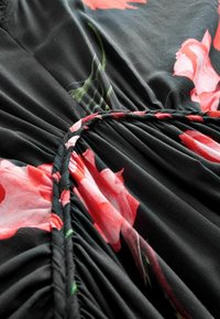 Zwarte stof met grote roze bloemenpatronen, met geplooide details en een gevlochten rand langs de rand. Focus op de textieldetails.