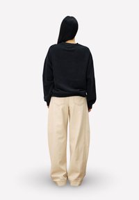 Zwarte oversized sweatshirt met een ronde hals, gecombineerd met beige, losse broek; gladde textuur en eenvoudig ontwerp.