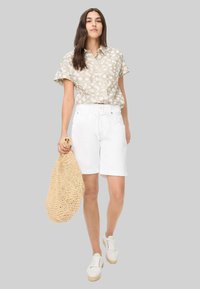 Lichtbeige bloemenkorte mouwen shirt, witte shorts met een strik taille en witte sneakers. Houdt een geweven rieten tas vast. Soepele texturen.