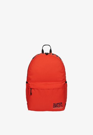Rode rugzak van een gestructureerd canvasmateriaal, met een afgeronde bovenkant, een voorvak met ritssluiting en zwarte merkopdruk. Voorzien van zwarte accenten aan de riemen en metalen onderdelen.