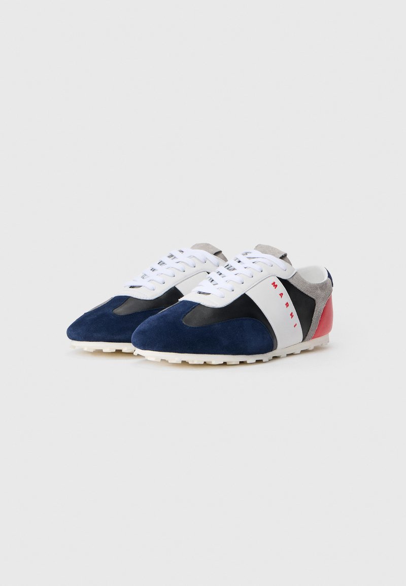 Marineblå og sorte ruskinds sneakers med hvide snørebånd, en rød og grå hæl, samt en struktureret gummisål. Har et iøjnefaldende hvidt stribe og logo.