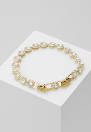 Bracelet en or avec des cristaux ronds et transparents sertis dans des chatons en or, reliés par une chaîne en or, présenté sur un bloc géométrique blanc.