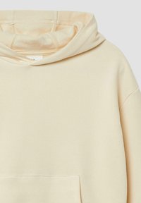 Beige hoodie met een grote buidelzak, zachte textuur en zichtbare stikdetails rond de capuchon en zoom.