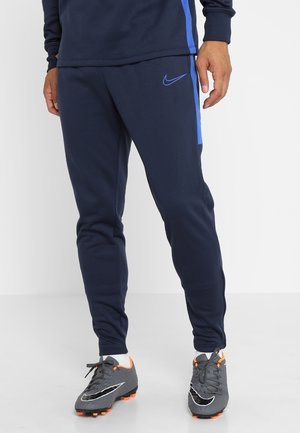 Granatowe dresy wykonane z miękkiego materiału o dopasowanym kroju. Mają jasnoniebieski pasek z boku i małe logo Nike z przodu.