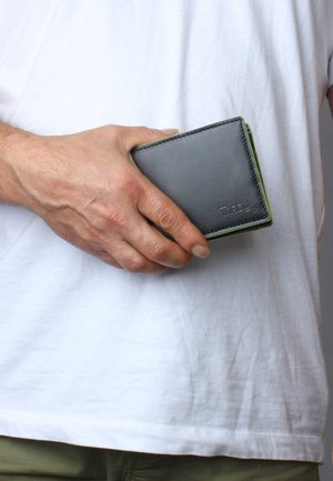 Portafoglio in pelle nera con accenti verdi, caratterizzato da una superficie liscia e bordi cuciti, tenuto in una mano su uno sfondo bianco semplice.