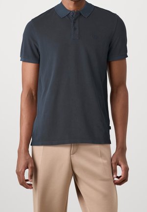 Polo azul marino oscuro hecho de algodón suave, con cuello abotonado, mangas cortas y un pequeño logo en el pecho izquierdo.