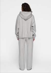 Grijze hoodie met een relaxte pasvorm, gecombineerd met bijpassende grijze trainingsbroek. De stof lijkt zacht met een gladde textuur.