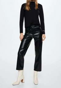 Schwarzes Langarm-Oberteil mit Stehkragen, kombiniert mit hoch taillierten, glänzenden schwarzen Kunstlederhosen im Krokodil-Look und cremefarbenen Stiefeletten mit Blockabsatz.
