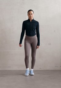 Fekete, hosszú ujjú, cipzáros felső, világosbarna leggings és világoskék sportcipő. Simára csiszolt anyagok, testhezálló design. Egyszerű, modern megjelenés.