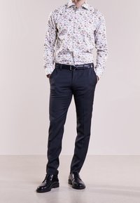 Camicia bianca a maniche lunghe con stampa animale multicolore, abbinata a pantaloni scuri e sagomati e scarpe in pelle nere.