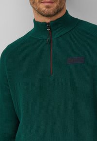 Grüner, gerippter Fleece-Pullover mit hohem Kragen, halbem Reißverschluss und einem navyblauen Markenpatch auf der Brust. Strukturierter Stoff mit enganliegender Passform.