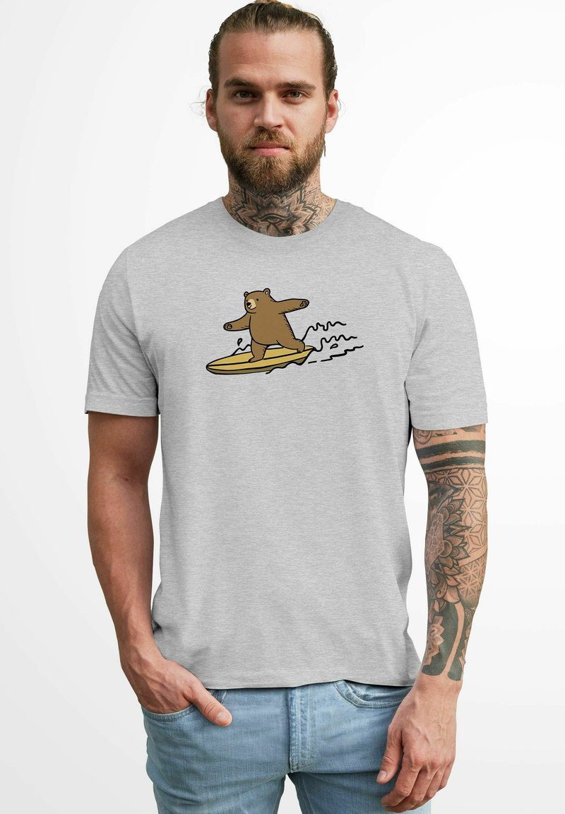 Hellgraues T-Shirt mit einem grafischen Motiv eines braunen Bären, der auf einem gelben Surfbrett surft. Das Design enthält schwarze Konturen und subtile Wellendetails.