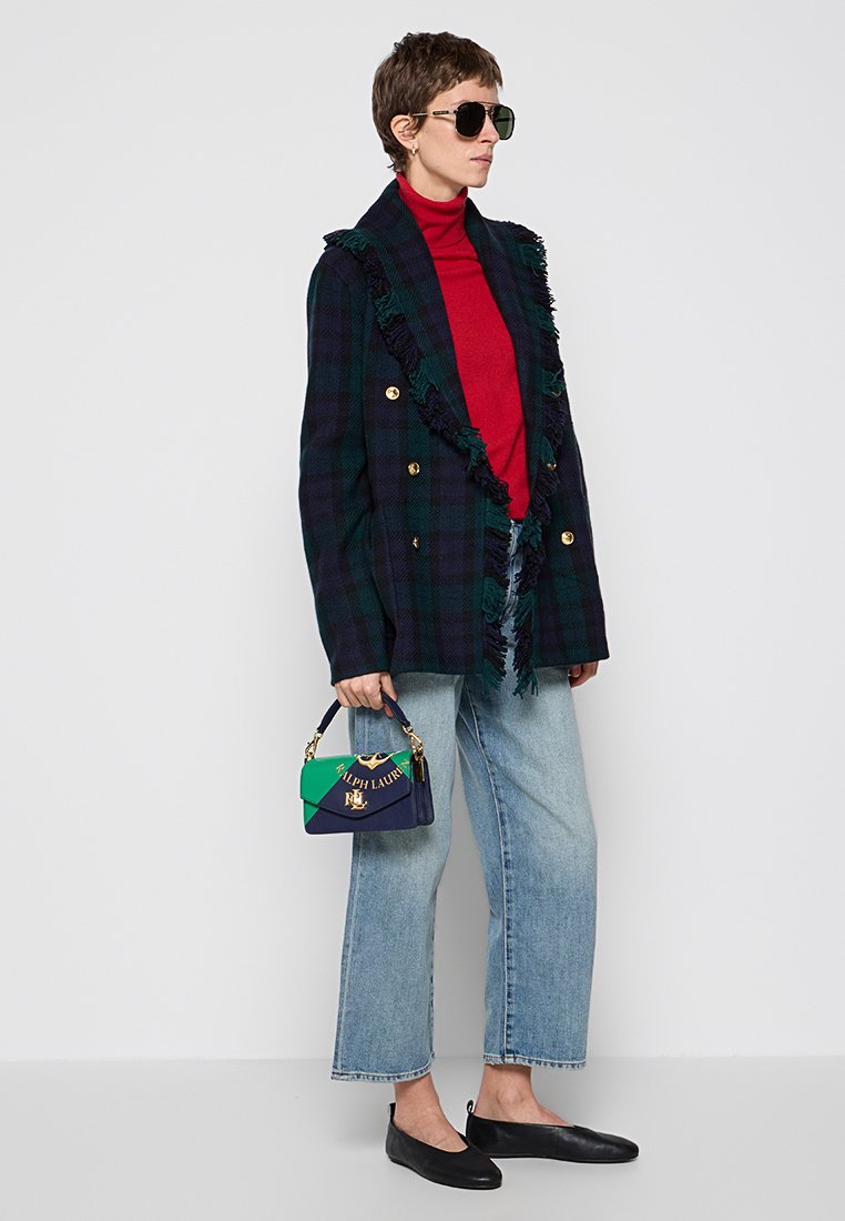 Dwurzędowa sportowa marynarka w kratę w ciemnozielonym i granatowym kolorze z postrzępionymi brzegami, czerwona golf, szerokie dżinsy i mała torebka w granatowo-zielonym kolorze.