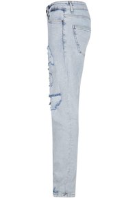 Jean en denim bleu clair usé, présenté de profil avec des déchirures sur la cuisse et une poche arrière visible.