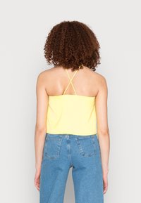 Top cropped amarelo com alças cruzadas nas costas, combinado com jeans de ganga azul de cintura alta. Textura suave, design casual.