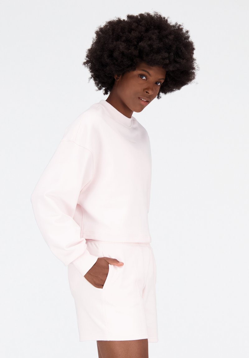 Sudadera corta de color rosa claro, con mangas largas, cuello redondo y bolsillos laterales, combinada con unos pantalones cortos a juego para un look cohesivo.