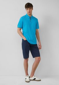 Turkusowa koszulka polo z zamkiem, w zestawie z granatowymi szortami i białymi trampkami z czarnymi akcentami. Gładka tekstura, casualowy wygląd.