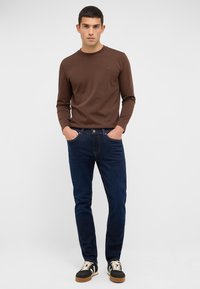 Brązowa bluzka z długim rękawem, granatowe dżinsy i czarne trampki z beżowymi akcentami. Slim fit, okrągły dekolt i przednie kieszenie w dżinsach.