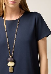 Navyblauw kortärmige jurk, van gladde stof met een ronde halslijn, gecombineerd met een meerkleurige hangerketting met drie gestileerde stenen.