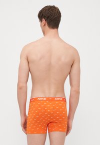 Narancssárga boxeralsó, fehér Nike logó mintázattal, rugalmas derekú, márkanevével, sima anyagból készült.