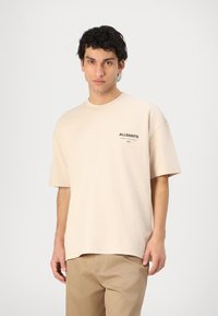 Beige cotton t-shirt with a relaxed fit, short sleeves, and a black "ALLSAINTS" logo on the left chest. Smooth texture, simple design.