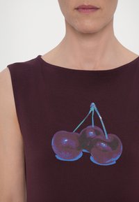 Burgundy sleeveless top featuring a graphic print of three cherries in shades of purple and blue, with a round neckline and soft texture.