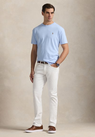 Šviesiai mėlynas trumpomis rankovėmis marškinėliai su apvalia iškirpte, balti džinsai, rudi sportbačiai. Marškinėliuose ant krūtinės yra mažas logotipas. Kasdienio stiliaus ir laisvo prigludimo.