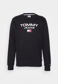 Sudadera negra con cuello redondo. Muestra "TOMMY JEANS" en texto blanco en la parte frontal, con un detalle de logo en bloques de color debajo.