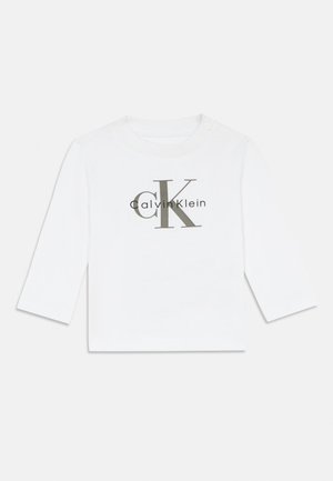 Bjela košulja dugih rukava s okruglim izrezom i detaljima na gumbima. Na prednjoj strani se nalazi sivi "CK" logo i tekst "Calvin Klein".