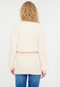 Cremiger, gestrickter Pullover mit aufwendigen Mustern, langen Ärmeln und tailliertem Design. Die strukturierte Oberfläche und der gerippte Saum schaffen visuelles Interesse.