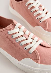 Paire de baskets en toile rose avec lacets blancs et semelles épaisses en caoutchouc blanc, montrées en gros plan sur un fond neutre.