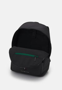 Zaino nero realizzato in tessuto resistente. Presenta una tasca anteriore con zip verde, chiusura con pattina superiore e un ampio interno.
