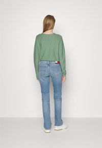 Suéter de punto verde, jeans ajustados azul claro con bolsillos traseros y una etiqueta de logo, combinados con zapatos blancos; textura suave, diseño casual.
