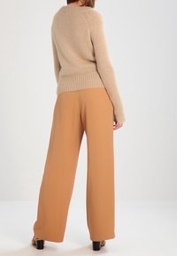 Beżowy, dziany sweter z długimi rękawami i luźnym krojem, w połączeniu z jasnobrązowymi spodniami z wysokim stanem i szerokimi nogawkami. Gładka tekstura, minimalistyczny design.