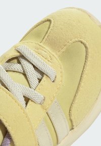 Yellow sneaker featuring a soft suede upper and mesh detailing, with light-colored laces and branding accents on the sides.
