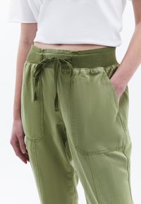 Pantalones verdes con cintura elástica y cordón, bolsillos laterales y detalles cosidos. La tela tiene una textura suave y un ajuste relajado.