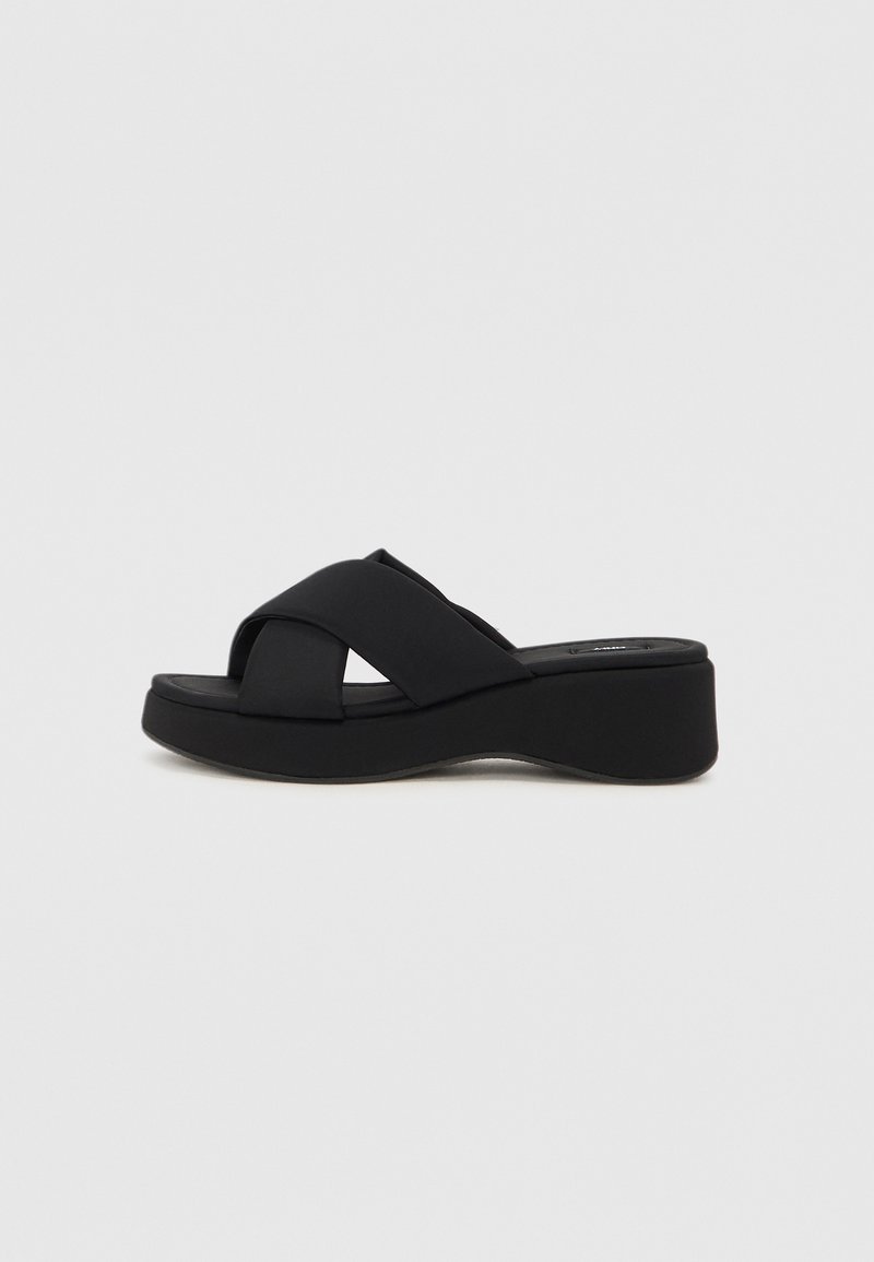 Black platform sandals with crossover strap design, made from soft material, featuring a thick sole and slight sheen.
