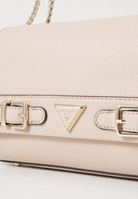 Beige tekstureret læder håndtaske med to gyldne spænder og et trekantet logo. Har en kædestropp og kontrasterende sort piping.