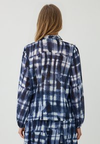 Blusa a quadri blu navy e bianca con maniche lunghe, colletto piegato e vestibilità comoda, realizzata in tessuto leggero e liscio.