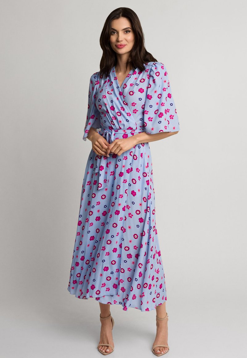 Jasnoniebieska sukienka w stylu kopertowym z krótkimi rękawami, z nadrukiem kwiatowym w kolorze różowym i fioletowym. Materiał jest zwiewny, z wiązaniem w talii.