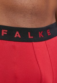 Boxers pour hommes rouges avec une ceinture élastique noire portant le texte "FALKE" en rouge. Fabriqués en tissu lisse avec des détails de coutures visibles.